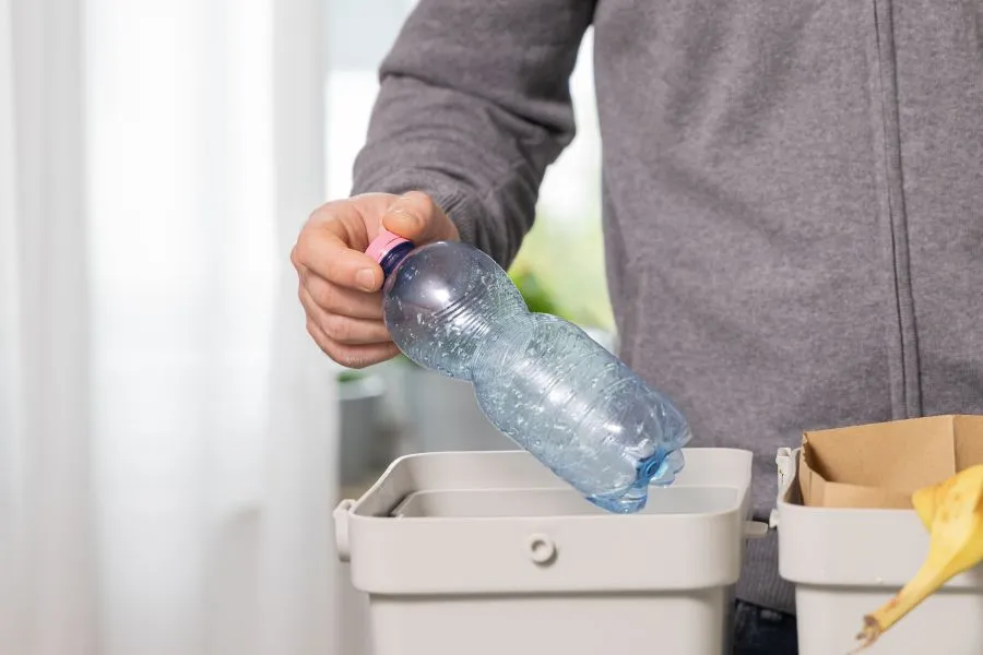 A person throwing a plastic bottle into a trash can