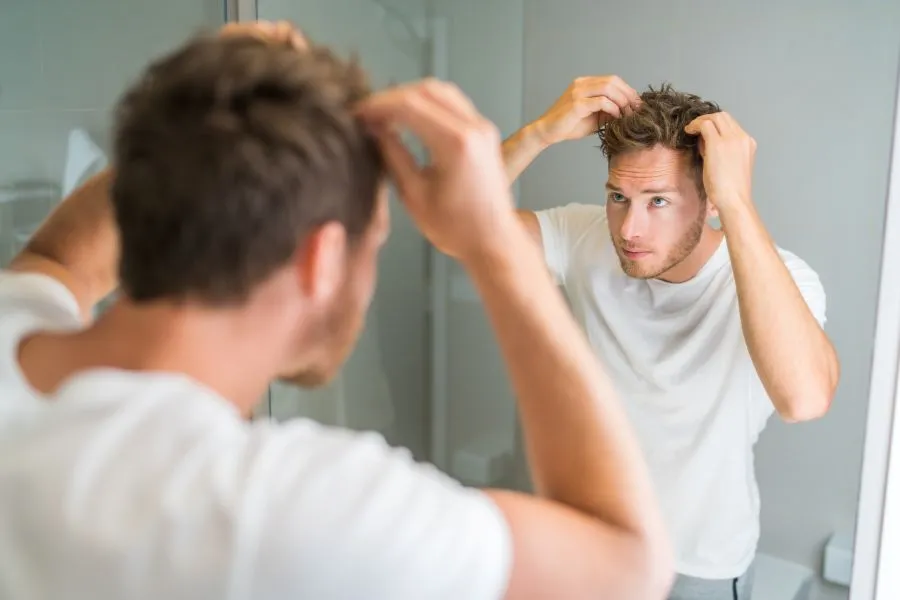 A man looking in the mirror inspecting his hair.