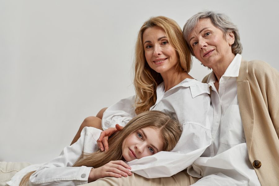 three generations of women sit together in an embrace. neutral expression or smiling at camera