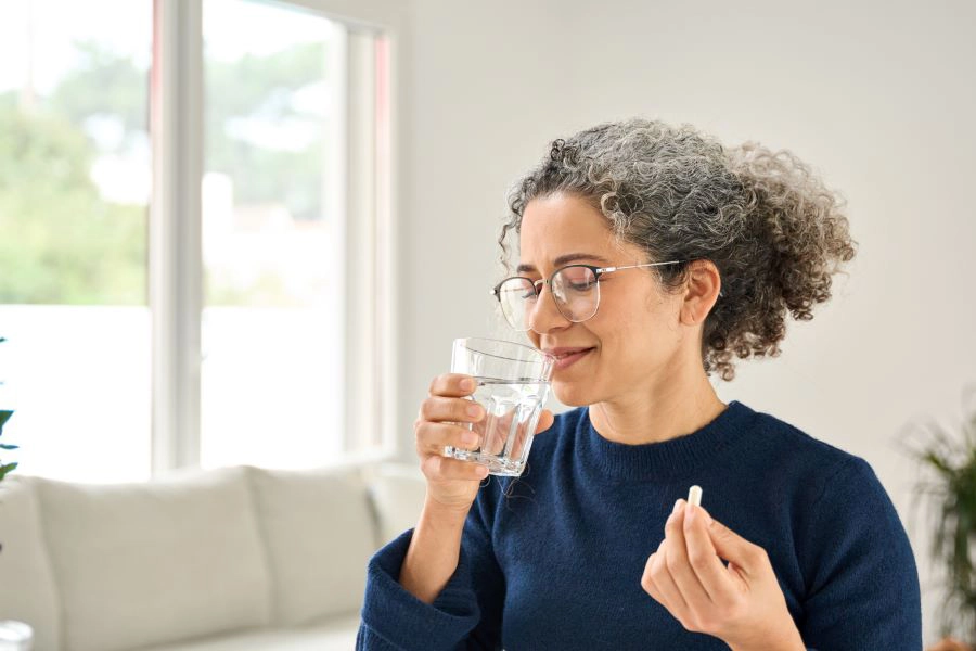 Happy healthy woman of middle age talking pill holding glass of water