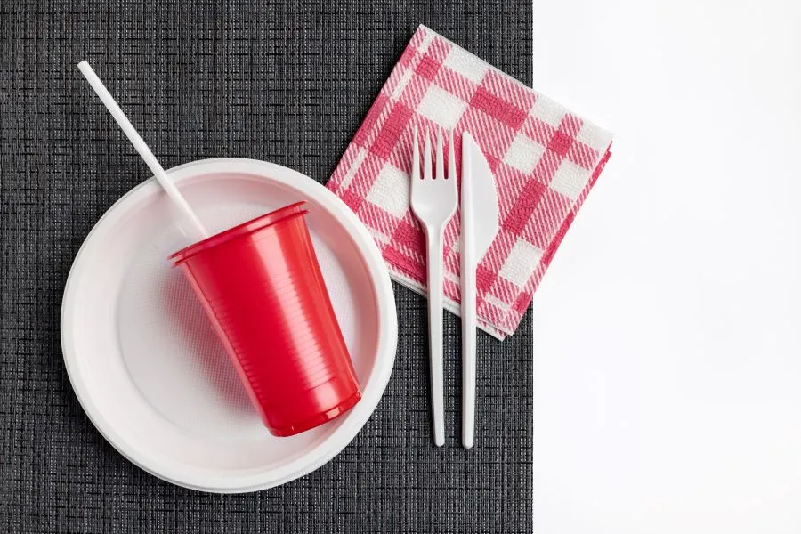 A plate and fork and knife with a red cup and a straw.